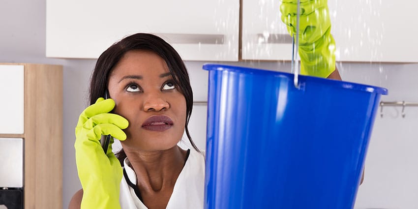 Woman holds up bucket as water comes from ceiling