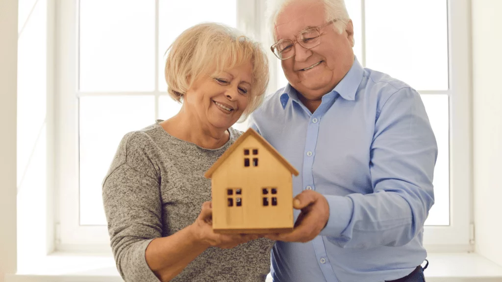 Two elderly holding a wooden house in their hands