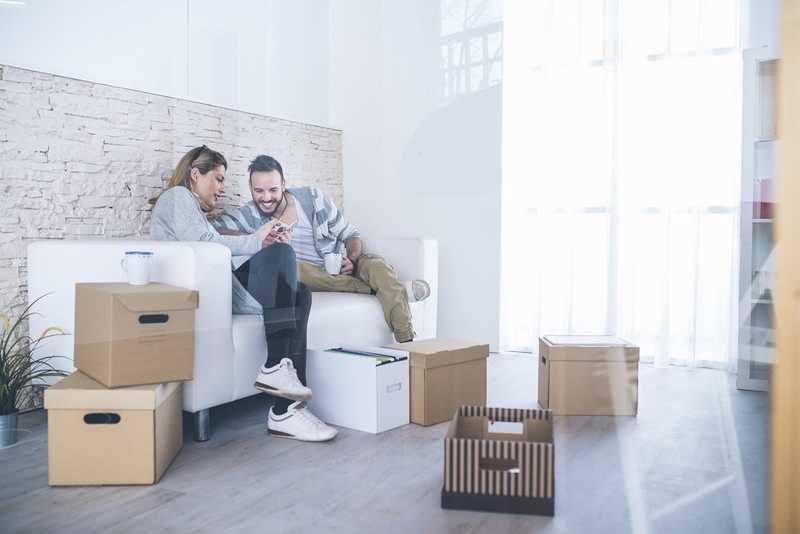 Two people look on a smartphone with cardboard boxes in their living room